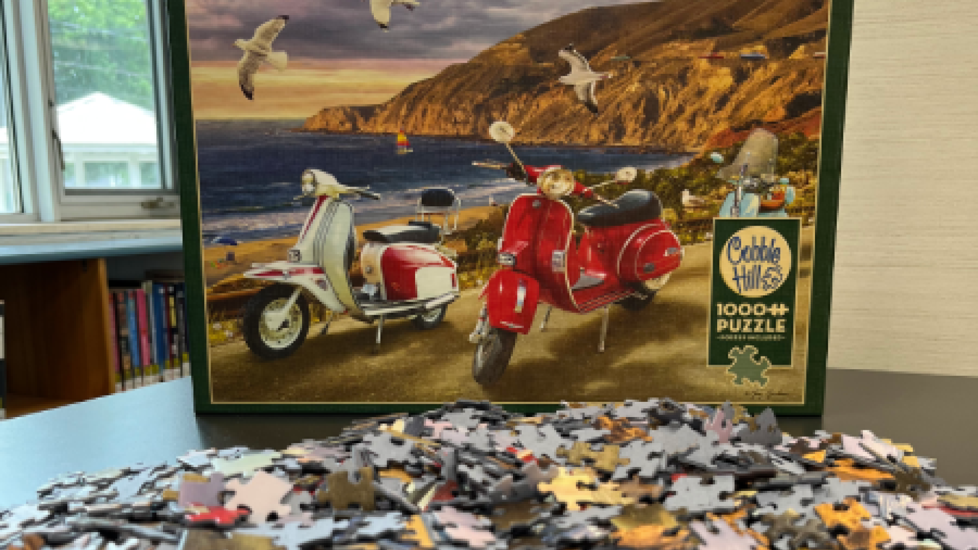 Puzzle pieces spread across a table with the box showing a beach scene with vespas behind them.