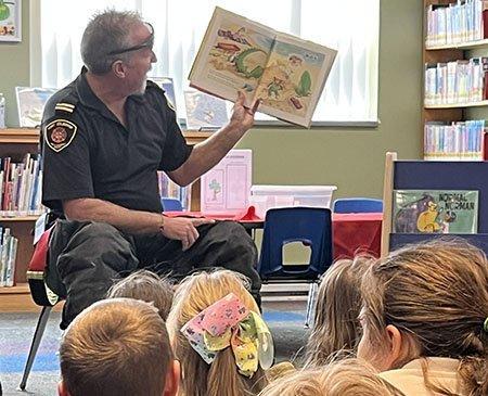 Image of a firefighter in uniform reading a story to a group of young children.
